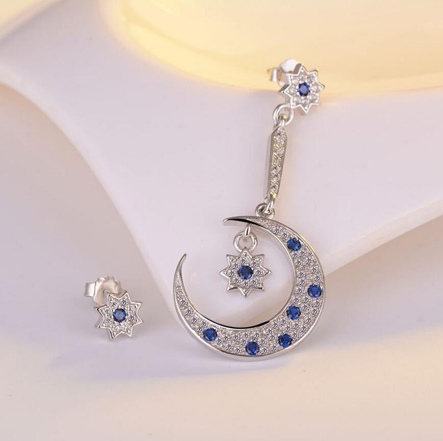 Asteria Asymmetrical Crystal Earrings - A pair of delicate star and moon themed silver earrings encrusted with blue and transparent crystals.