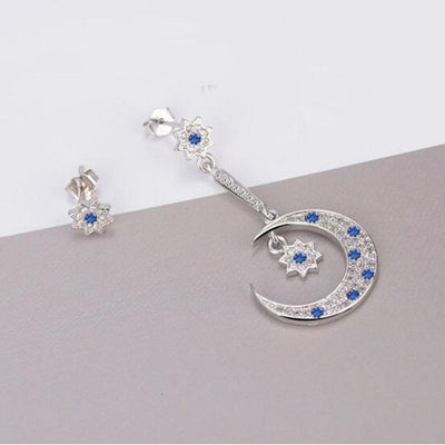 Asteria Asymmetrical Crystal Earrings - A pair of delicate star and moon themed silver earrings encrusted with blue and transparent crystals.