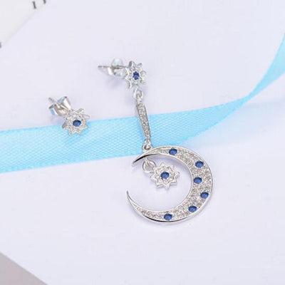Asteria Asymmetrical Crystal Earrings - A pair of delicate star and moon themed silver earrings encrusted with blue and transparent crystals.