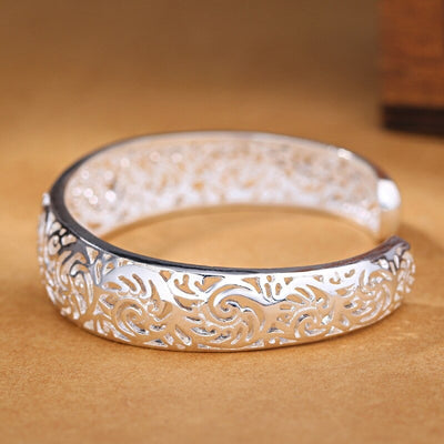 Jocasta Cut-Out Silver Cuff Bangle - An elegant yet chunky silver cuff with a floral/vine-like cut-out pattern, made from bright silver.