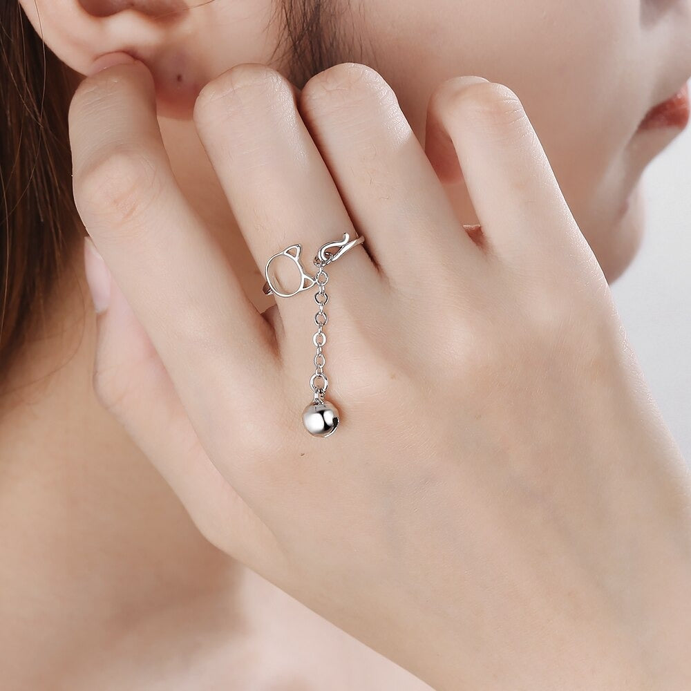 Tinklebell Silver Cat Bell Ring - An adjustable silver ring with a cat head charm on one side, and a small bell attached to a length of chain. 