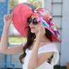 Heavenly Hibiscus Reversible Sunhat - A lovely, brightly-coloured large-brimmed sunhat with a solid colour on one side and a complimentary floral print on the other, which can be worn either way. It has a detachable scarf. This image shows a model wearing the Salmon colour, which is a sort of orangy-peachy-pink.
