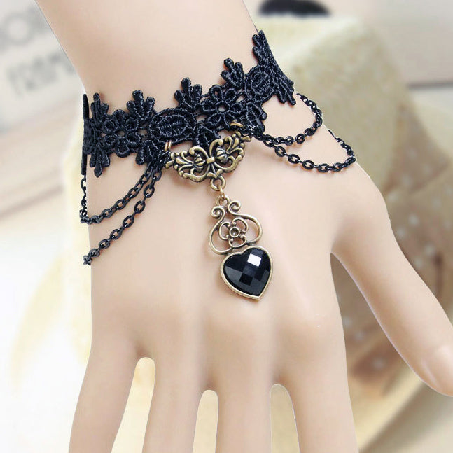 The Magdalene Cuff - A black lace bracelet adorned with metal hardware, chains, and a black heart motif.