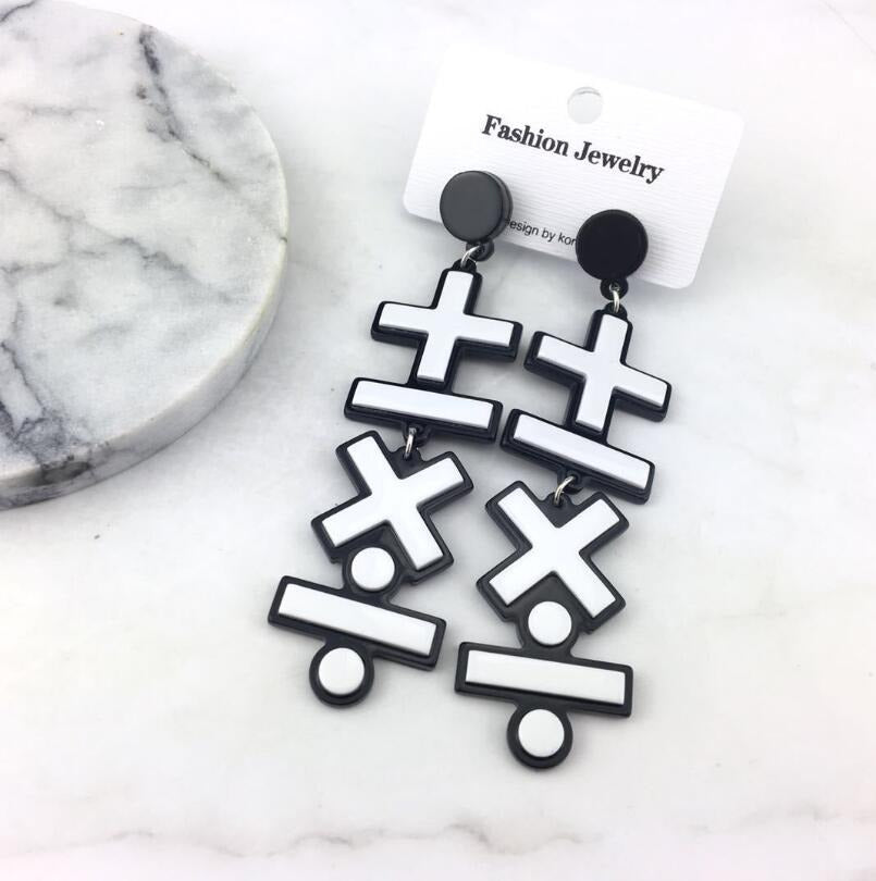 Retro Revival Mathematician Earrings - Long dangly earrings with mathematics symbols, plus, minus, times, and divide. They are white plastic with a black plastic background, to make it look like they have a cartoon-style outline.